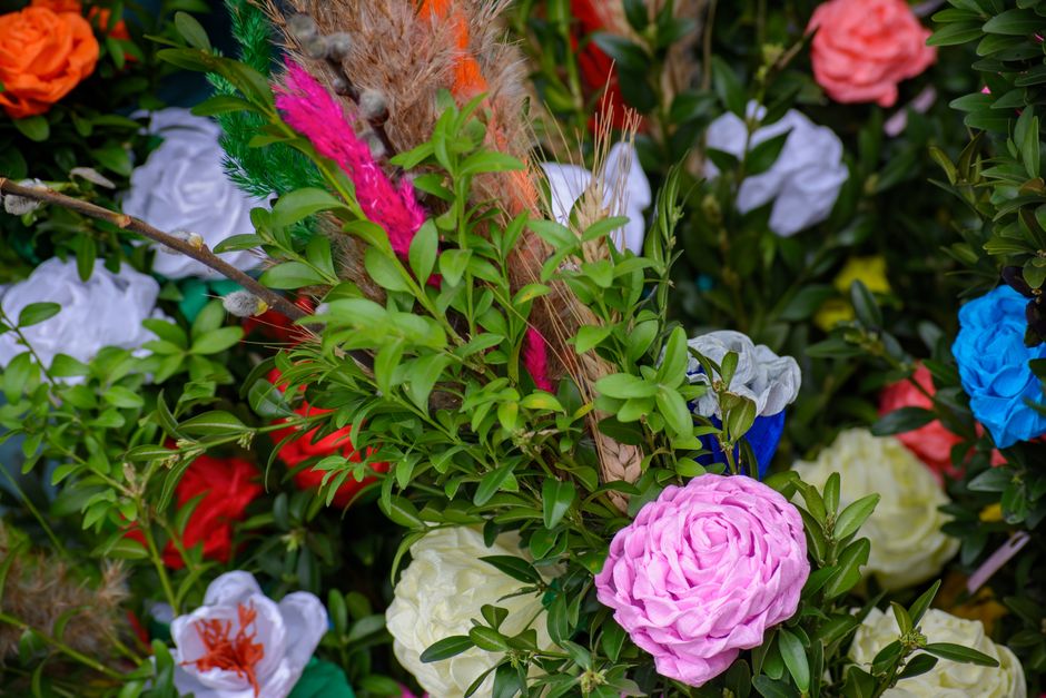 A vibrant floral arrangement featuring a variety of fresh flowers including a prominent pink ranunculus, white and orange lilies, bright blue and red roses, and other colorful blooms, all nestled amon
