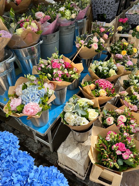 A display of freshly arranged floral bouquets on a blue table, featuring a variety of pastel-colored flowers including pink roses, white hydrangeas, and light green foliage, wrapped in brown craft pap